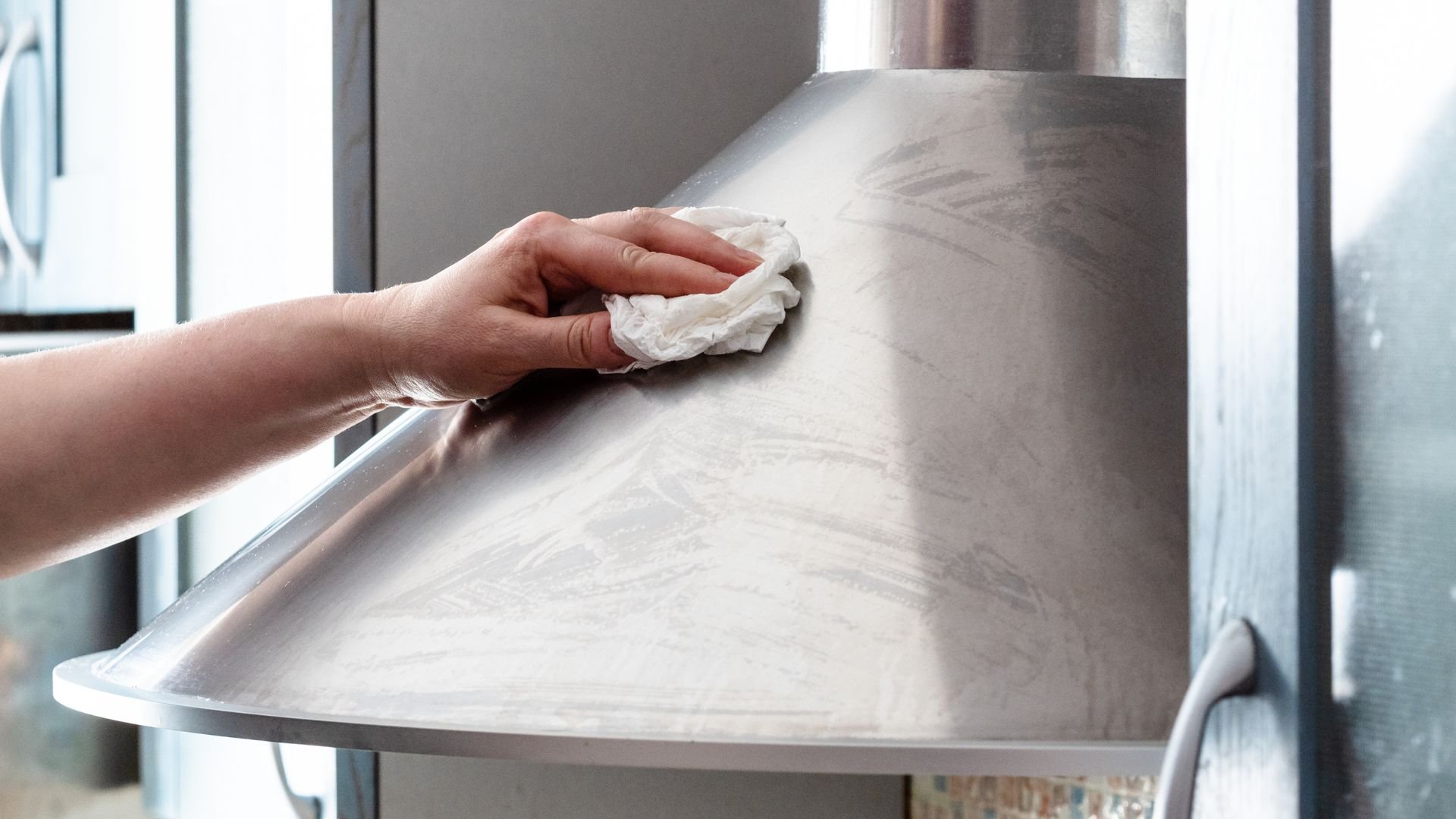Hand wiping clean stainless steel surface with white cloth